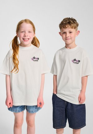 Vita bomull t-shirts med korta ärmar, med en blommönster i rosa och svart på bröstet, kombinerat med denimshorts.