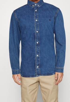 Camicia in denim di colore blu scuro con maniche lunghe, colletto alla francese, bottoni frontali e un logo discreto sul petto. Tessuto liscio.
