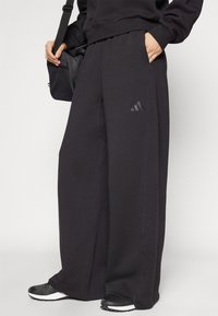 Juodos plačios kelnes iš minkštos medžiagos, su elastinga juosmeniu, šoninėmis kišenėmis ir subtiliu Adidas logotipu kairėje pusėje.