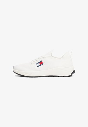 Zapatilla blanca de punto con suela negra, cordones en la parte delantera, lengüeta en el talón y logo de Tommy Jeans en el lateral.