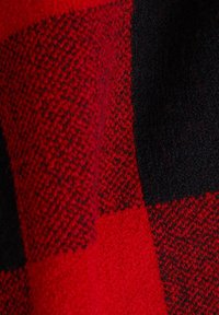 Gros plan sur un tissu en laine épais à carreaux rouges et noirs avec un motif tricoté texturé.