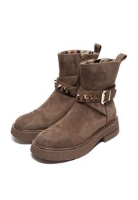 Botas de tobillo de ante marrón con suela de goma texturizada, una correa con tachuelas y un forro interior con estampado. Incluye cremalleras laterales para facilitar su uso.