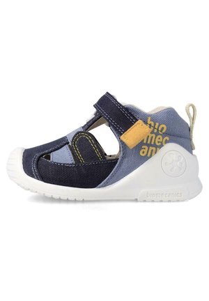 Sandalia de tela en azul marino y celeste con suela de goma blanca, cinta de velcro, detalles recortados y un parche de acento amarillo.