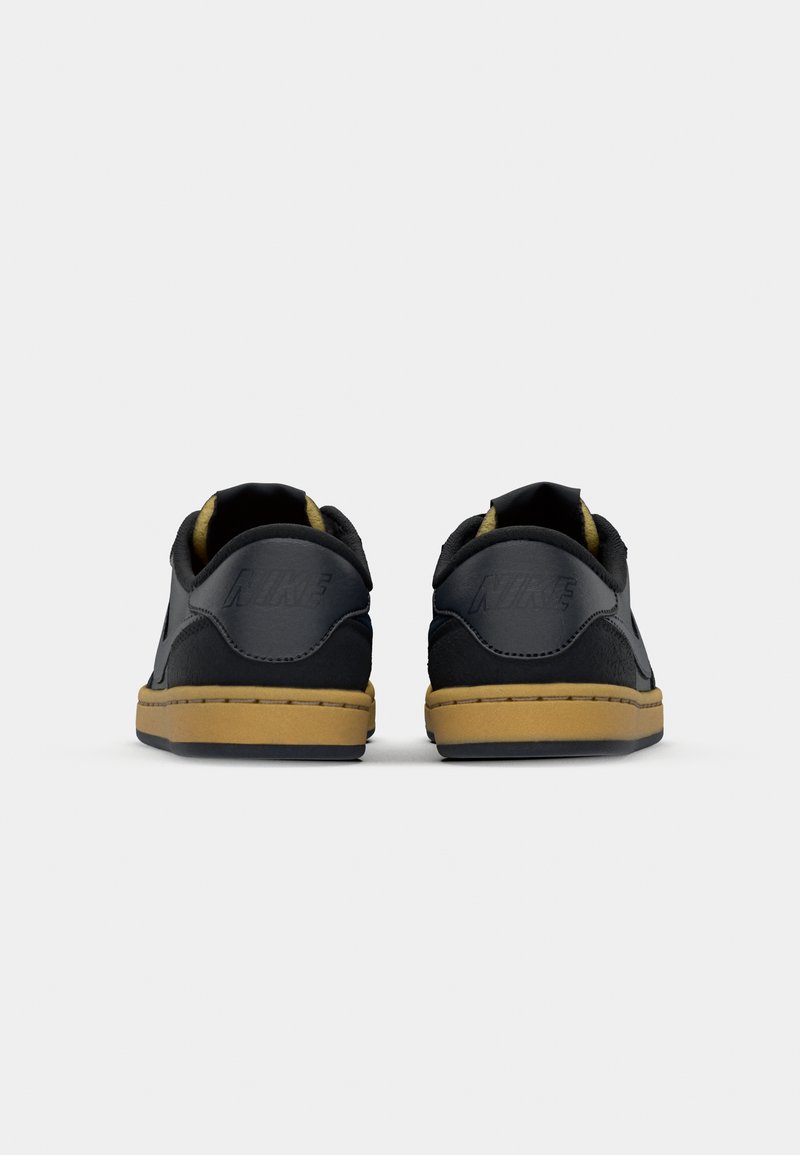 Baskets en cuir noir avec des accents en suède, semelles plates en caoutchouc et une semelle extérieure marron. Présente un logo Nike au talon. Design arrondi.