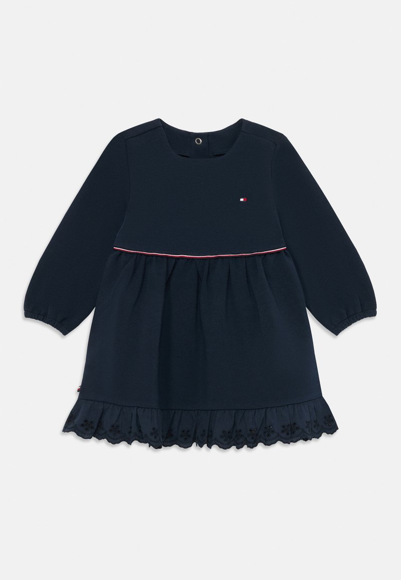 Námornícky modré šaty s dlhým rukávom, okrúhlym výstrihom, červeným a bielym akcentom na pás, a volánkovým lemom s čipkovým detailom a kvetinovými výrezmi.