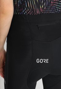 Svarta leggings med GORE-logotyp, slät textur, förstärkt sömnad och en liten dragkedja bak för förvaring.