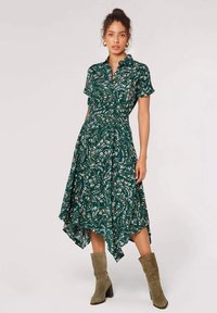 Groene jurk met korte mouwen, kraag en asymmetrische zoom. Heeft een wit bladerenpatroon en hangt soepel met een zachte textuur.