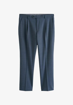 Ciemnoskóra ręka spoczywająca obok dopasowanych niebieskich spodni garniturowych i białej, wsuniętej w spodnie koszuli z długim rękawem.