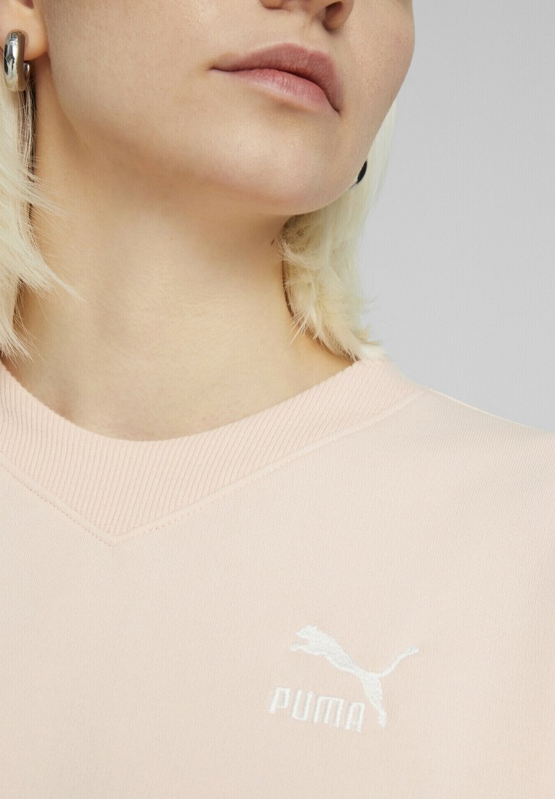 Felpa rosa chiaro con design a V, colletto ribbed e logo Puma ricamato bianco sul petto. Tessuto morbido.
