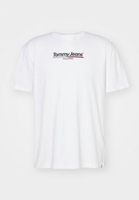 Camiseta blanca de algodón con cuello redondo, que presenta un logo impreso "Tommy Jeans" en negro y rojo en el pecho. Manga corta, corte regular.