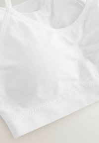 Vit bomullssportbh med en mjuk textur, bred elastisk band och sydda detaljer. Har tunna justerbara axelband och en sömlös design.