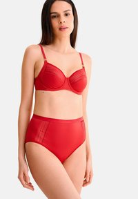 Rood lingerie set bestaande uit een gevoerde bh met onderdraad en doorschijnende details, gecombineerd met high-waisted slipjes. Gladiant textuur overal.