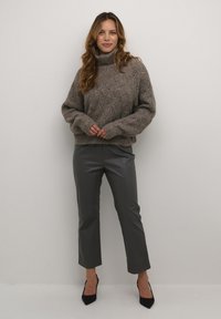 Chunky knitted brown sweater with a high collar, paired with gray cropped faux leather pants and black pointed-toe heels.