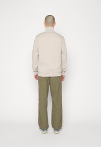 Beige pullover med hög krage, långa ärmar och elastiska muddar, kombinerad med lösa, olivgröna byxor och neutrala sportskor.