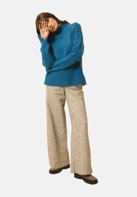 Niebieski sweter z dzianiny o wysokim dekolcie i prążkowanym wykończeniu, w połączeniu z szerokimi beżowymi spodniami z korduroy. Czarne, solidne obuwie dopełnia zestaw.