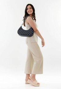 Borsa nera con design trapuntato e tracolla intrecciata, abbinata a un top beige e pantaloni larghi, caratterizzati da una texture liscia.