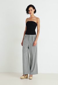 Top nero senza spalline abbinato a pantaloni a gamba larga a righe grigio chiaro e scarpe con piattaforma in legno chiaro. Tessuti morbidi e vestibilità rilassata.