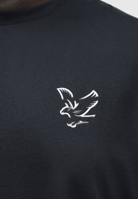 Μαύρο μπλουζάκι με λευκό γραφικό που απεικονίζει ένα πουλί σε πτήση στην αριστερή περιοχή του στήθους.
