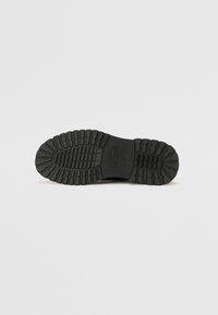 Black rubber sole with deep treads, featuring a smooth surface and raised patterns for grip. Size marked as 37 on the side.
