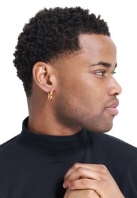 Boucle d'oreille en or, d'épaisseur moyenne, finition polie, portée à l'oreille gauche. Sujet habillé d'un pull col roulé noir, apparaissant de profil.