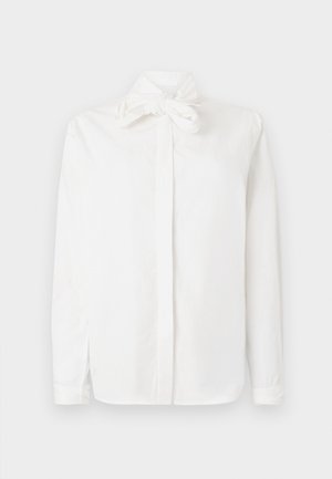 Cămașă albă cu mâneci lungi, confecționată din bumbac, având un detaliu cu nod la guler, cu închidere cu butoni și slituri laterale. Textură netedă.