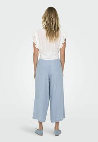 Blusa ligera, blanca, con mangas acampanadas combinada con pantalones de pierna ancha en azul claro. Tejido suave y corte relajado. Diseño simple y casual.