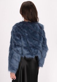 Giacca corta in finta pelliccia blu navy con maniche lunghe e una texture morbida e shaggy, abbinata a una gonna in satin nera.