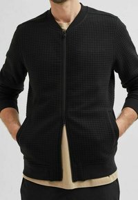 Černá bomber bunda s texturovanou tkaninou, plným zipem, žebrovanými manžetami a dvěma bočními kapsami. Jednoduchý design s moderním, strukturovaným střihem.
