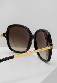 Ochelari de soare supradimensionați din scoică cu lentile gradient maro și accente din metal aurit. Prezintă rame unghiulare și branding "MICHAEL KORS" pe braț.
