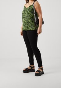 Vihreä ja musta zebramaalauksellinen toppi, mustat kapeat housut ja massiiviset mustat remmisandaalit. Koristeina musta käsilaukku ja hopeaketju.