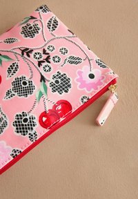 Blommönstrad påse i rosa, med svarta och röda detaljer, röd dragkedja och gyllene hårdvara. Slät tygtextur.