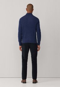 Granatowy sweter w warkoczowy wzór z wykończeniem z prążkowanego materiału, w parze z ciemnymi spodniami slim fit. Tkanina ma teksturowany wygląd w jednolitym kolorze.