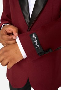 Burgundy suit jacket with a black satin lapel. Features a white shirt cuff and a tag with "OPPOSUITS®" on the sleeve. Textured fabric.
