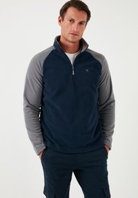 Navy blue fleece pullover with gray raglan sleeves, half-zip design, and a small logo on the upper left side. Soft texture, casual fit.