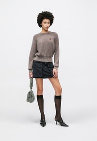 Helepruun soonikuga kampsun ümara kaelusega, sellega sobitatud tume teksase mini seelik, põlvekõrgused sokid ja mustad teravate ninadega kontsad.