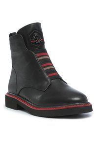 Bottines en cuir noir avec un emblème hexagonal, détail élastique rouge et marron rayé, et semelle en caoutchouc texturé avec accent rouge.