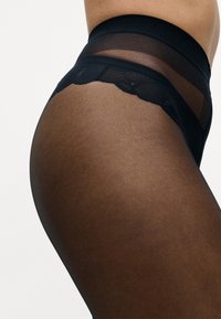 Sorte gennemsigtige strømpebukser med en glat overflade, bølget talje og en tætsiddende design, der fremhæver benets form.
