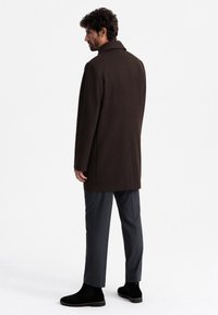 Brown wool coat with a tailored fit, featuring a notched collar. Gray trousers and black ankle boots complete the outfit.