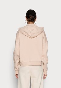 Cropped hoodie rosa chiaro in tessuto morbido, con un ampio cappuccio e maniche a vestibilità rilassata, polsini e orlo a costine. Texture liscia, design minimale.