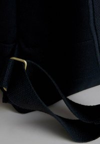 Borsa di stoffa nera caratterizzata da una superficie testurizzata, una lunga tracolla regolabile e dettagli in metallo dorato. Il design enfatizza la durabilità e la praticità.