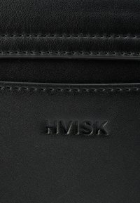 Mala preta de couro com logótipo "HVISK" em relevo. Apresenta textura suave, costuras discretas e design minimalista. Forma compacta e elegante.