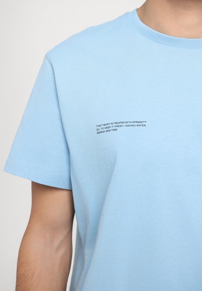 Lyseblå bomulds T-shirt med rund halsudskæring. Har lille sort trykt tekst foran om PPRMNT oliebehandling for friskhed.