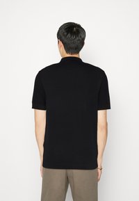 Černé polo tričko s krátkým rukávem a texturovaným pleteným vzorem na rukávech. Disponuje klasickým límcem a přiléhavým střihem.