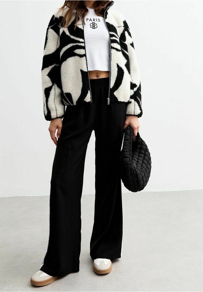 Giacca in fleece con motivo astratto nero, base bianca; design cropped con zip. Abbinata a pantaloni larghi neri e sneakers bianche.