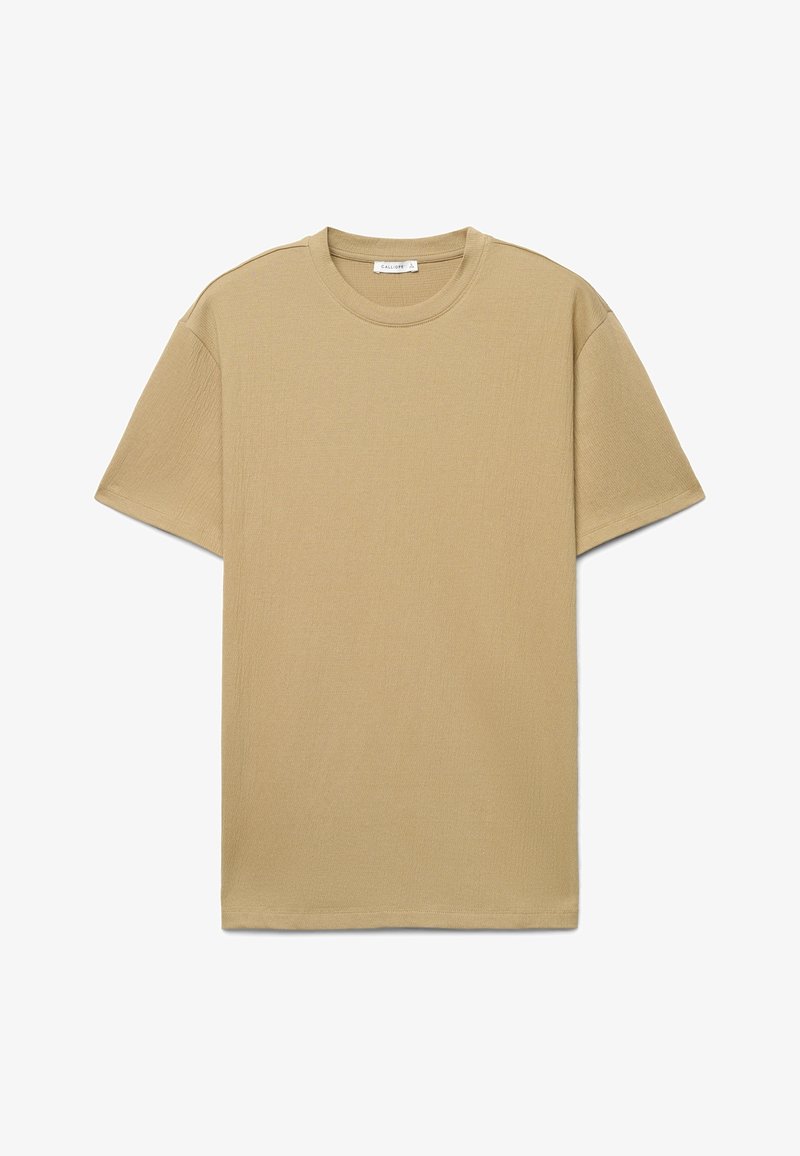 T-shirt beige à manches courtes avec col rond, en tissu subtilement texturé et une petite étiquette à l'intérieur de l'encolure.