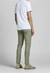 Biała koszulka polo z krótkim rękawem, jasne zielone spodnie o fakturze oraz beżowe buty zamszowe, pokazane od tyłu.