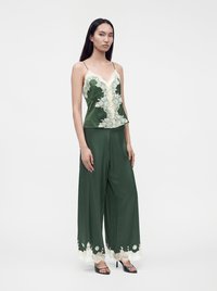 Femme portant un caraco en satin vert foncé avec des détails en dentelle crème et un pantalon large assorti avec une bordure en dentelle, debout sur fond blanc.