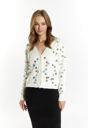 Maglione bianco con scollo a V, impreziosito da paillettes circolari colorate di diverse dimensioni. Tessuto con texture e design aderente. Gonna nera.
