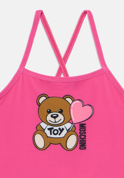 Canottiera rosa con una grafica di un orsetto dei cartoni animati che tiene un palloncino a forma di cuore, con il testo "TOY MOSCHINO" in grassetto nero.