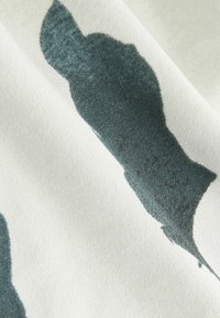 Gros plan sur un tissu blanc avec des formes abstraites irrégulières gris foncé imprimées à la surface, mettant en valeur la texture et les détails du motif.